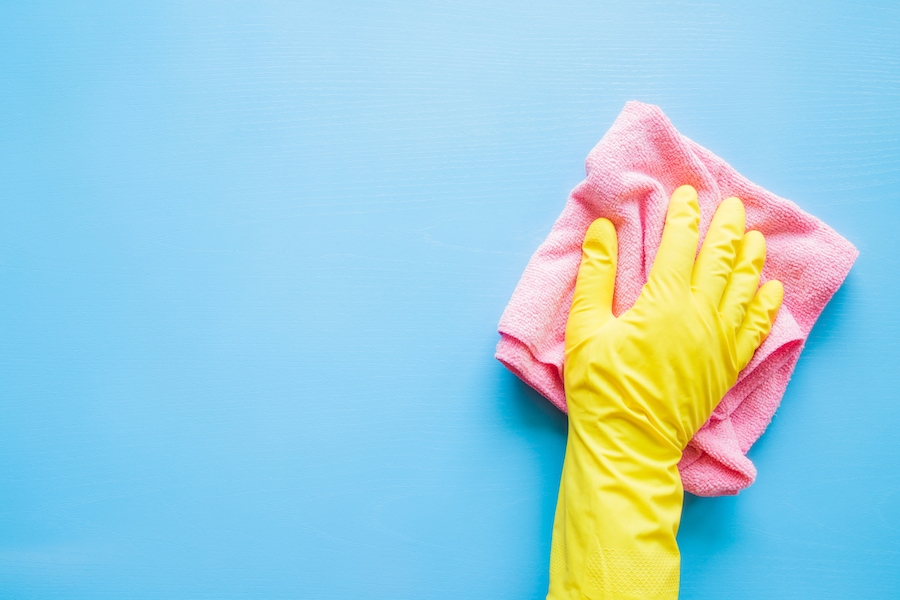 Yellow gloved hand washing a blue wall with a pink rag.